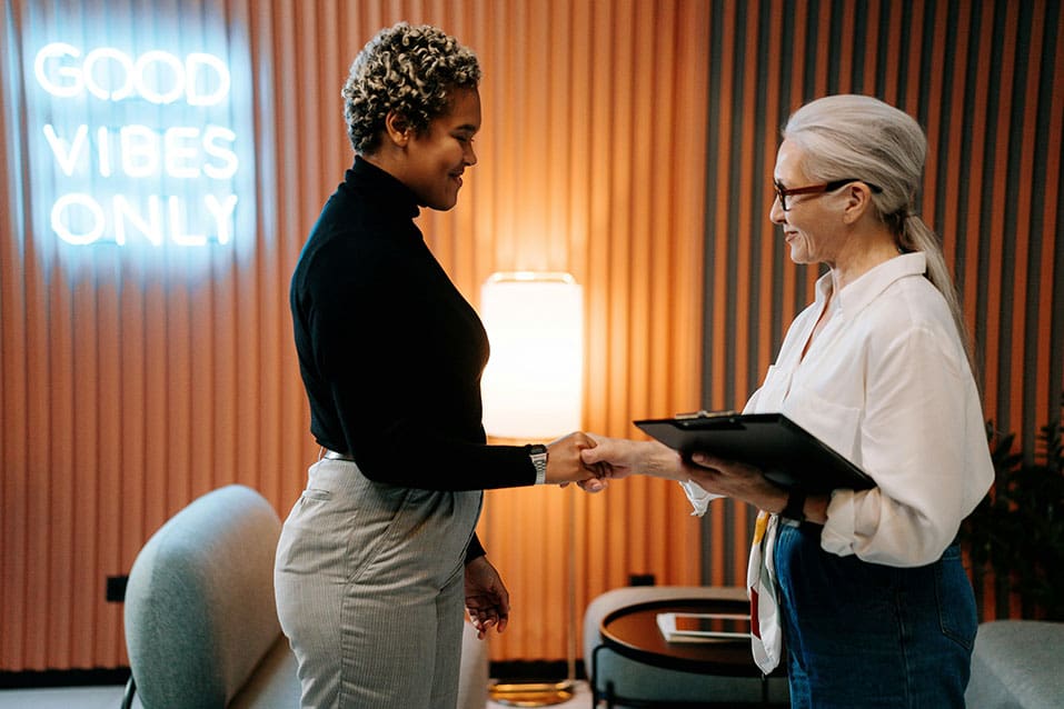 Two women shaking hands in a room.