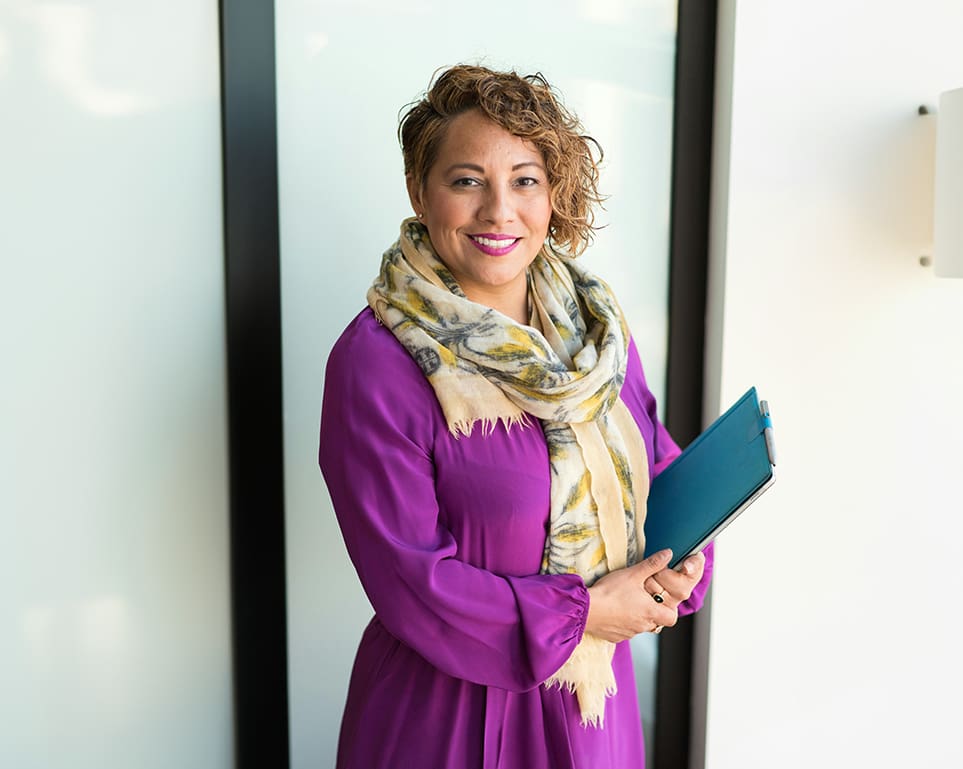 A woman in purple dress holding a blue book.